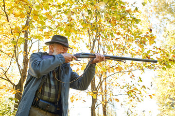 Concentrated hunter holding rifle and waiting for prey, hunter shooting in autumn forest. Hunting...