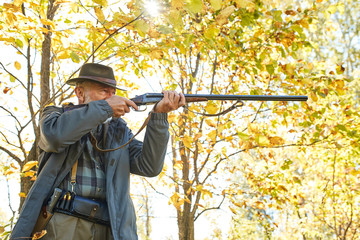 Concentrated hunter holding rifle and waiting for prey, hunter shooting in autumn forest. Hunting season