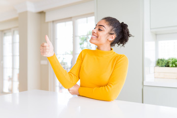 Beautiful african american woman with afro hair wearing a casual yellow sweater Looking proud, smiling doing thumbs up gesture to the side