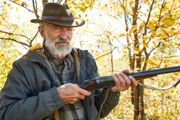 Senior caucasian hunter jolding shotgun ready to shoot on wild animals, shoot on bird in forest.