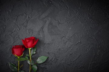 Red roses are placed on a black textured background. A sign of condolence, sympathy loss. Space for your text