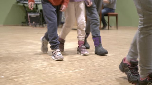 Close up low angle view of diverse young children's feet & shoes walking on wooden studio flooring.