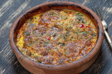 Ceramic bowl with vegetable frittata, simple vegetarian food. Frittata with tomato, pepper, onion and cheese on wooden table, close up. Italian egg omelette