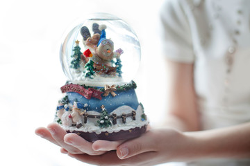 Snow globe with a snowman in the hands of a girl. White background.