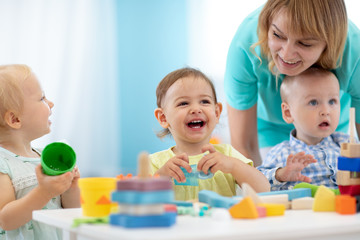 Babies play with teacher in nursery or creche - obrazy, fototapety, plakaty