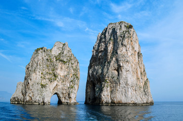 Fototapeta na wymiar The picturesque cliffs of Faraglioni near the island of Capri on a background of blue sea and sky.