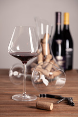 Crystal red wine glass, bottles, corkscrew, opener, sommelier knife, transparent decanter, corks on wooden table. Closeup, vertical, selective focus side view. Concept degustation winery cellar