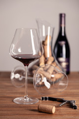 Crystal shiny red wine glasses, bottle, corkscrew, opener, sommelier knife, transparent decanter with corks on wooden table. Closeup, vertical, selective focus, side view. Concept wine magazine photo