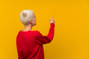 Teenager girl with white short hair over yellow wall pointing back with the index finger