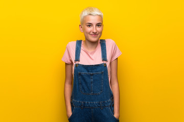 Teenager girl with overalls on yellow background laughing