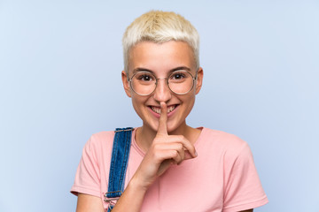 Teenager girl with overalls on blue wall doing silence gesture