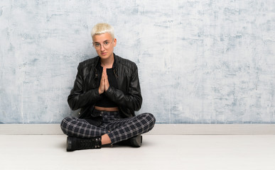 Young woman sitting on the floor keeps palm together. Person asks for something