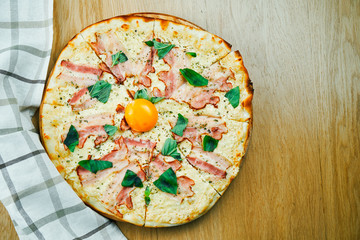 Italian, homemade carbonara pizza with yolk and bacon on a wooden table. Top view food with copy space. Flat lay