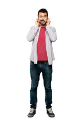 Fototapeta premium Full-length shot of Handsome man with beard frustrated and covering ears over isolated white background