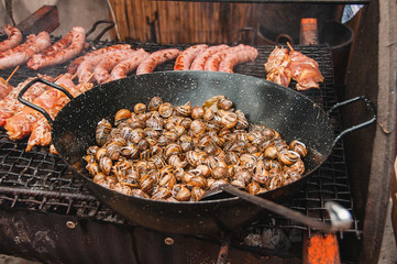 Traditional Mediterranean Snail Recipe and barbecue with sausages and meat on skewers . Tasty and freshly cooked hot snails and meat, smoke is visible.