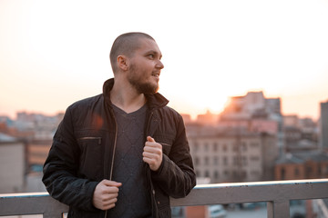 young handsome man looking to the side at sunset and smiling at the background of the city