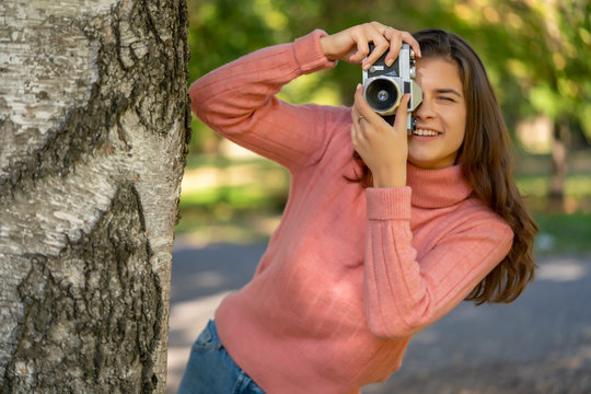 Young woman taking a picture photo with old style camera outdoor in the park.