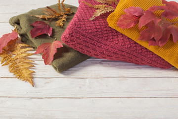 stack of sweaters with autumn leaves  on  white wooden table