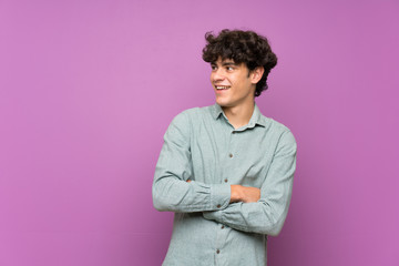Young man over isolated purple wall happy and smiling