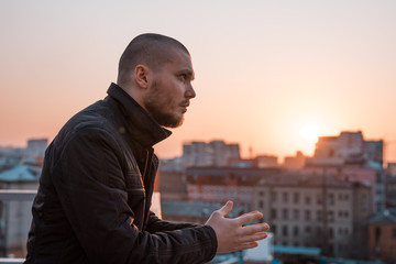 young handsome serious man looks away on the background of the city at sunset