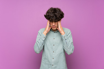 Young man over isolated purple wall with headache