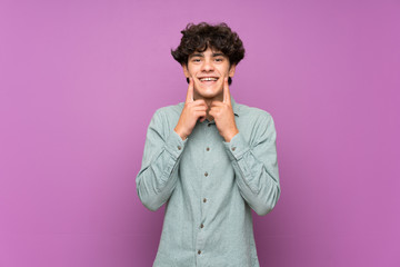 Young man over isolated purple wall smiling with a happy and pleasant expression