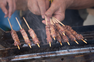 Man cooking marinated meat, Pork meat grilling on wooden skewer, outdoor grill with smoke coming up from the fire below. close up
