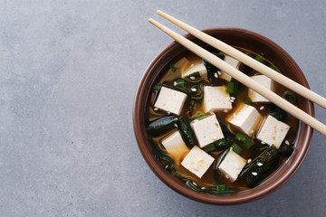 Bowl with miso soup and chopsticks on a gray background.