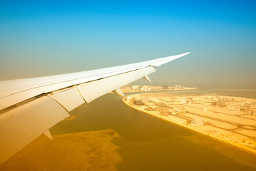 Fototapeta na wymiar Plane wig in the sky with desert city and ocean over sky background in Bahrain