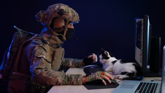 a man in a military uniform special forces sitting at the monitor and on the table is a cat