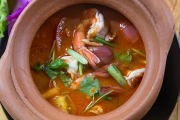 Tom yam Kung (Traditional spicy soup, tomato, lemongrass and galangal) /Thai hot spicy soup with shrimp in the clay pot on wood table background/