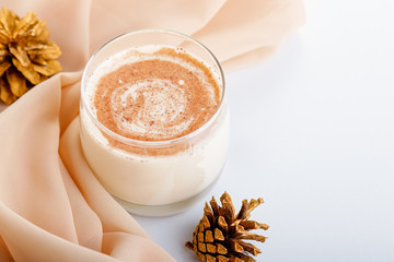 Traditional Christmas cocktail Eggnog with eggs, alcohol, grated nutmeg and cinnamon closeup, copy space, vertical frame. Sweet traditional drink on grey table with beige decorations and pine cones