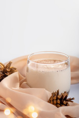 Traditional Christmas cocktail Eggnog with eggs, alcohol, grated nutmeg and cinnamon closeup, copy space, vertical frame. Sweet traditional drink on grey table with beige decorations and pine cones