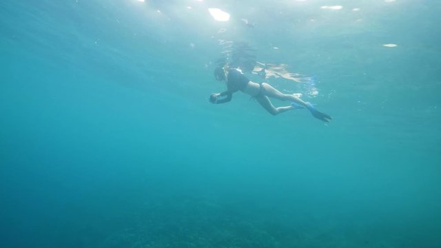Snorkeling woman with a smartphone enjoys shooting videos of underwater world.