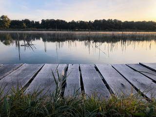 Wood masonry on the lake. Morning with light fog. Rotten pier on the shore of a calm reservoir. Shore reflection.