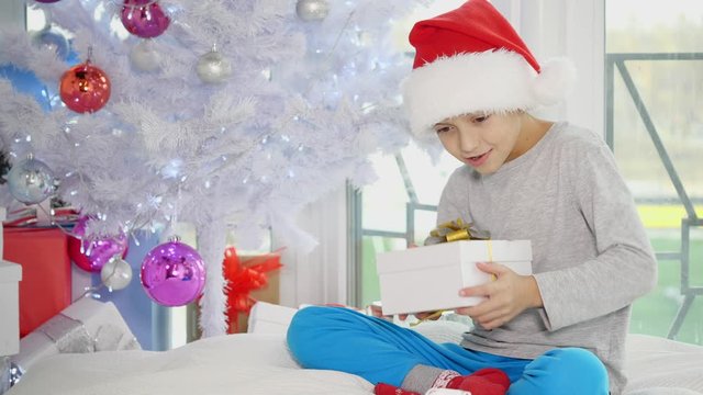 Funny video of curious boy taking Christmas presents from under the tree, shaking, knocking, listening, trying to find out what is inside.