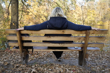 A girl sits on a bench against the background of a lake and autumn forest. Girl resting on a bench in the autumn forest in front of the lake.