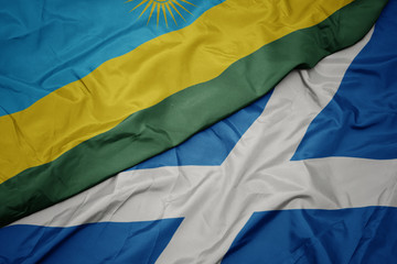 waving colorful flag of scotland and national flag of rwanda.