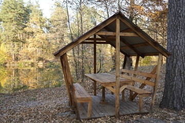 Wooden arbor in the autumn forest near the lake.