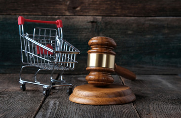 Consumer rights concept, judge hammer and grocery cart on vintage wooden background.