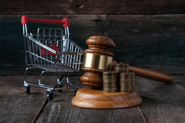 Consumer Protection Concept. Judges hammer, grocery cart and coins on  wooden background.