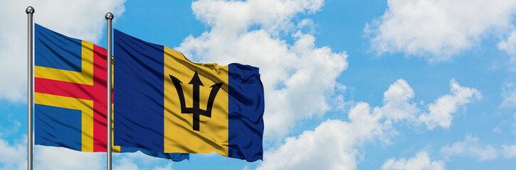 Aland Islands and Barbados flag waving in the wind against white cloudy blue sky together. Diplomacy concept, international relations.