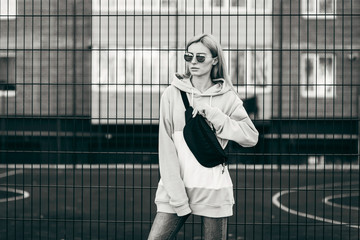 Stylish model girl at the city in a grey hoodie and glasses with waist bag