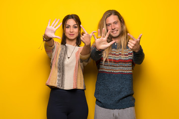 Hippie couple over yellow background counting seven with fingers