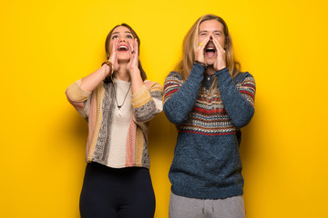 Hippie couple over yellow background shouting and announcing something