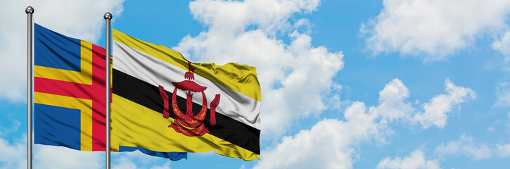 Aland Islands and Brunei flag waving in the wind against white cloudy blue sky together. Diplomacy concept, international relations.