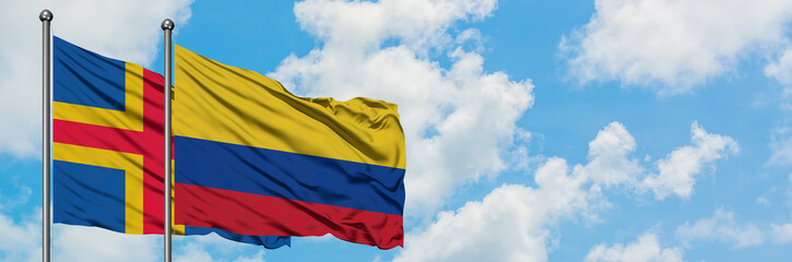 Aland Islands and Colombia flag waving in the wind against white cloudy blue sky together. Diplomacy concept, international relations.