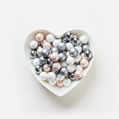 Christmas decorative colorful white, pink, grey balls in plate shape of heart on white background. Top view. Xmas concept. Isolated.