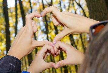 Close-up of mother and her son make heart shape with hands in autumn forest. 