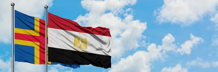 Aland Islands and Egypt flag waving in the wind against white cloudy blue sky together. Diplomacy concept, international relations.